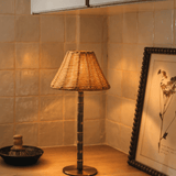 The Raffles cordless lamp glowing warm in a kitchen corner, its wicker shade on a bamboo stem and solid brass base