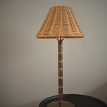 Cordless wicker shade lamp with a bamboo stem and brass base, unlit, on a dark side table against a farrow and ball mouses back wall
