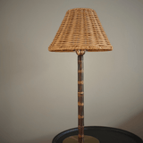 Cordless wicker shade lamp with a bamboo stem and brass base, unlit, on a dark side table against a farrow and ball mouses back wall