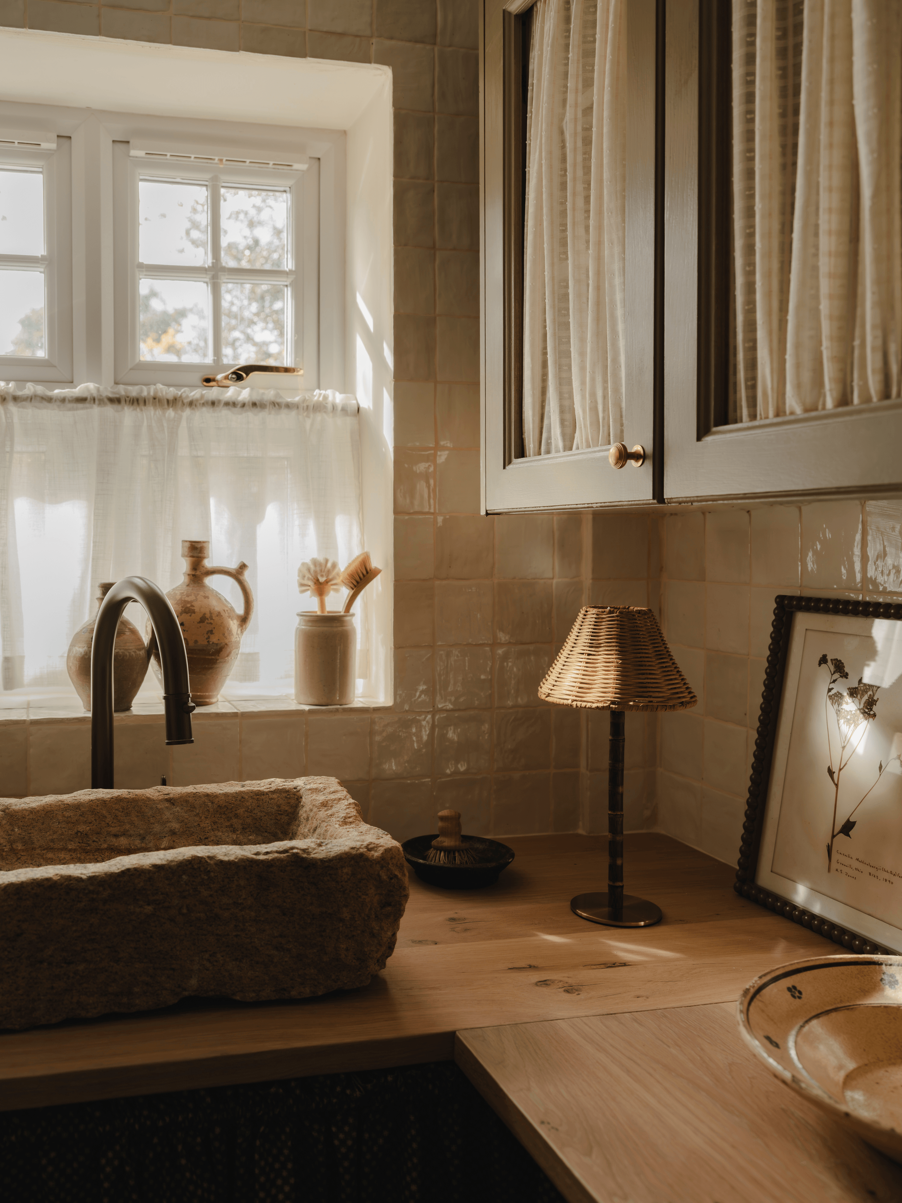 The Raffles lamp in a kitchen corner by the window, with a stone sink, ceramic bowl and framed botanical print