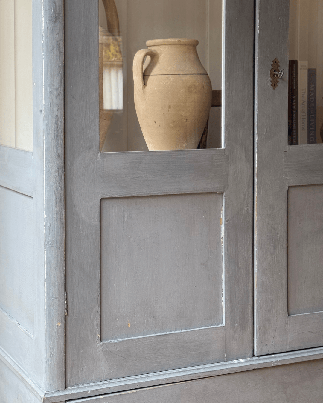 A close-up of an antique wooden cabinet or door with a small window showing a beige ceramic vase inside.
